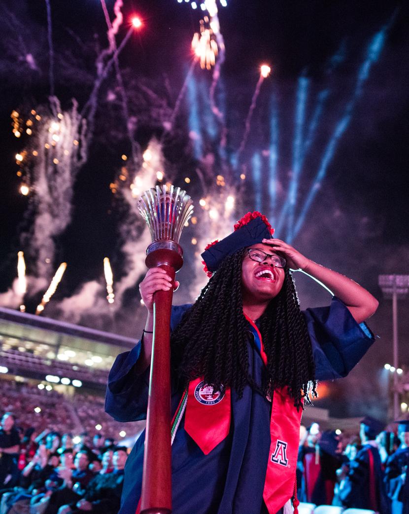Graduate holding the ceremonial torch with fireworks in the background