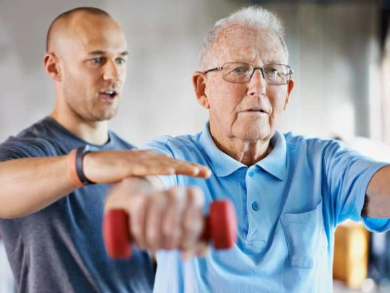 physical therapist training with elderly man with weights