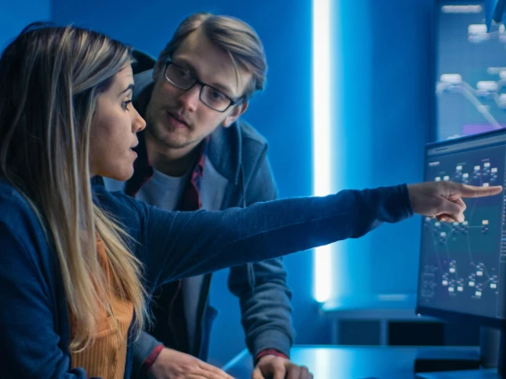 Woman pointing at computer screen while co-worker is talking with her