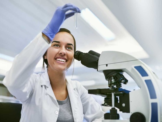 student scientist looking at vial in front of microscope 