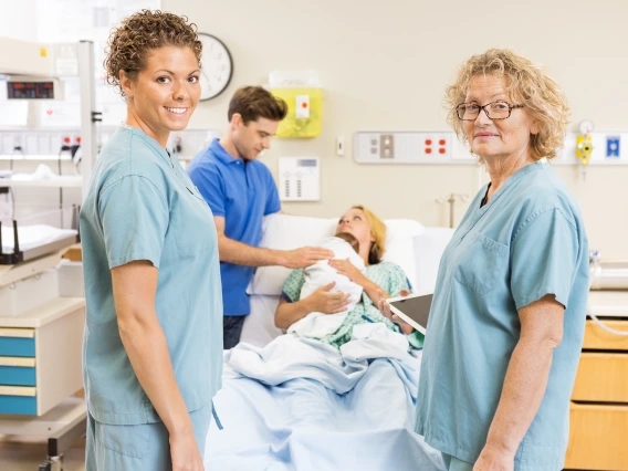 two adults standing in scrubs standing in front of coupled who just delivered a child. 