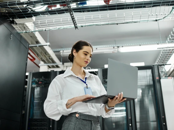 Photo of a woman working on a laptop while standing in a hallway.