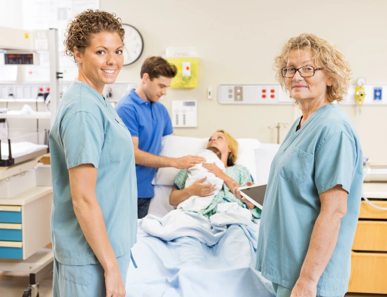 two adults standing in scrubs standing in front of coupled who just delivered a child. 