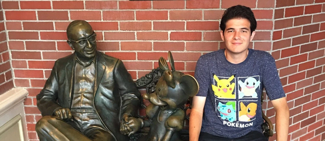 Sean Fagan sitting on a bench with a statue of Walt Disney in Tokyo Disneyland