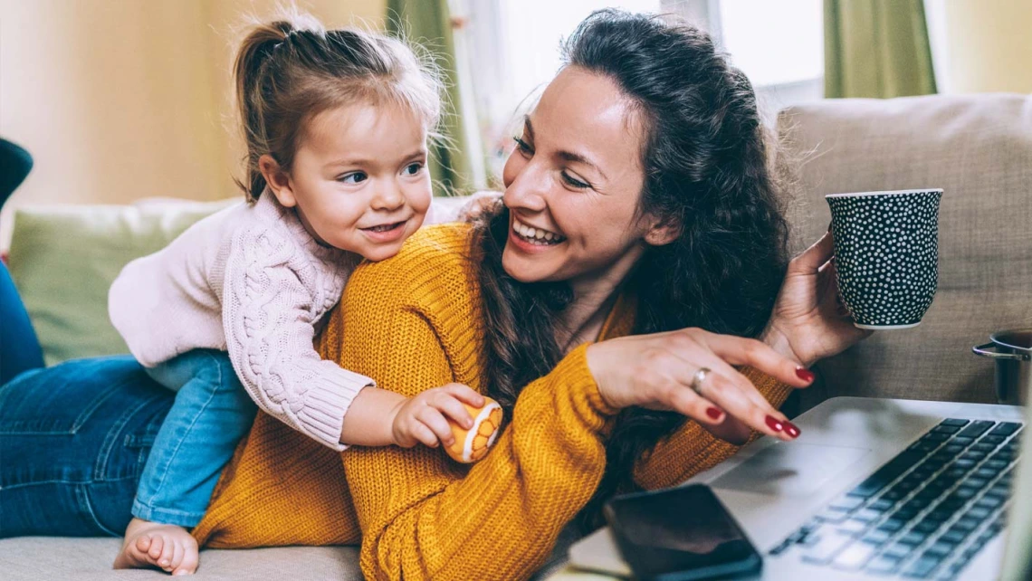 Woman playing on laptop with her daughter on her back