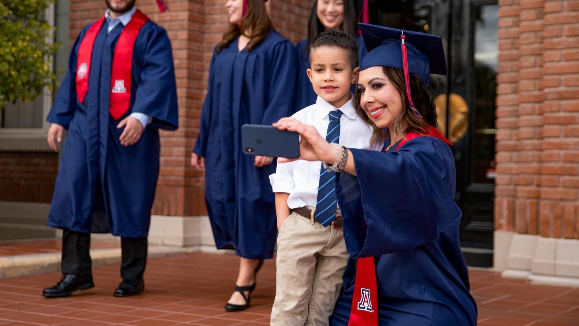 Mom in graduation cap and gown taking a photo with son