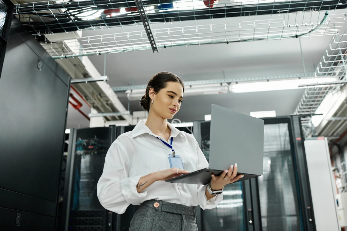 Photo of a woman working on a laptop while standing in a hallway.