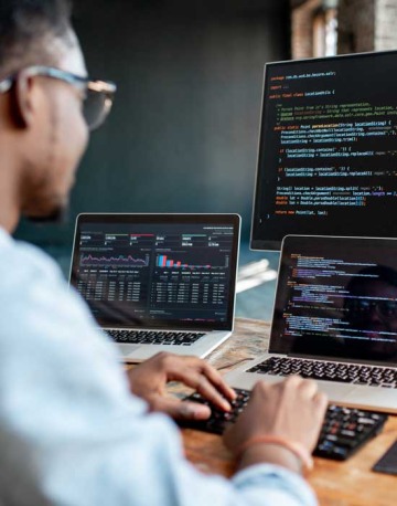 man working on laptop with multiple monitors of code