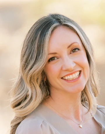 Headshot of a long haired, blonde woman smiling in a neutrally-toned top.