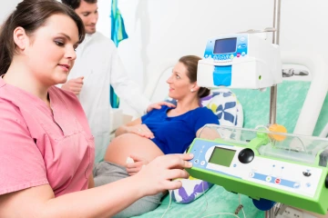 Delivery nurse checks vitals of pregnant woman who is standing next to a man.