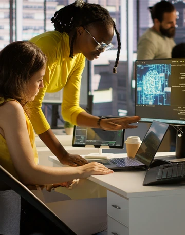 Two professionals leaned over a computer talking about information on the screen.