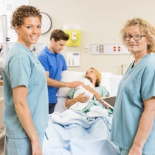 two adults standing in scrubs standing in front of coupled who just delivered a child. 