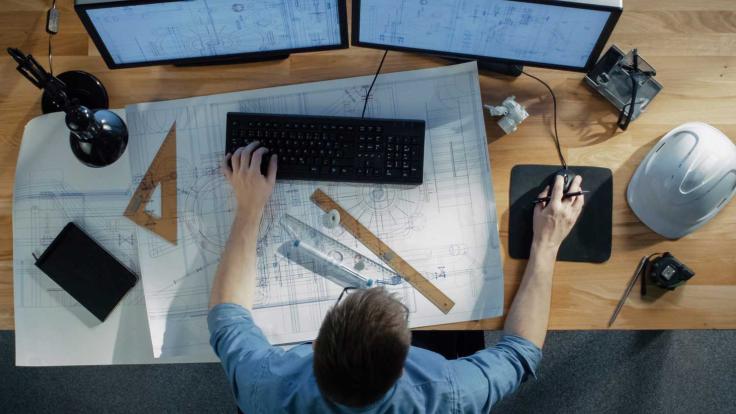 Man working on computer with blueprints spread across desk