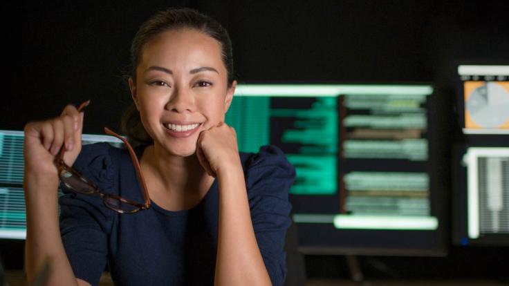 Woman Smiling with computer screens behind her