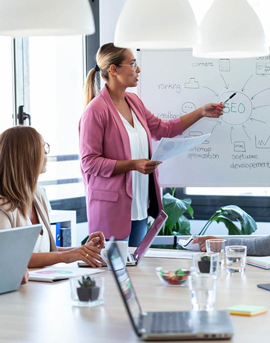 business woman pointing at white board during meeting with colleagues 