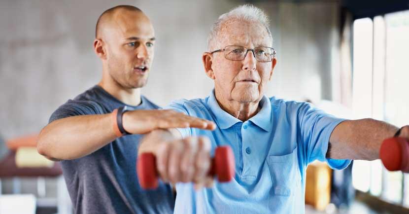 physical therapist training with elderly man with weights