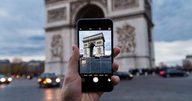 A person holds a cell phone to photograph the Arc de Triomphe in Paris